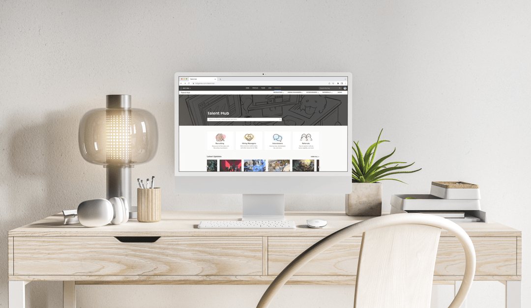 The Riot Talent Hub home page on a desktop monitor, on a light wooden desk